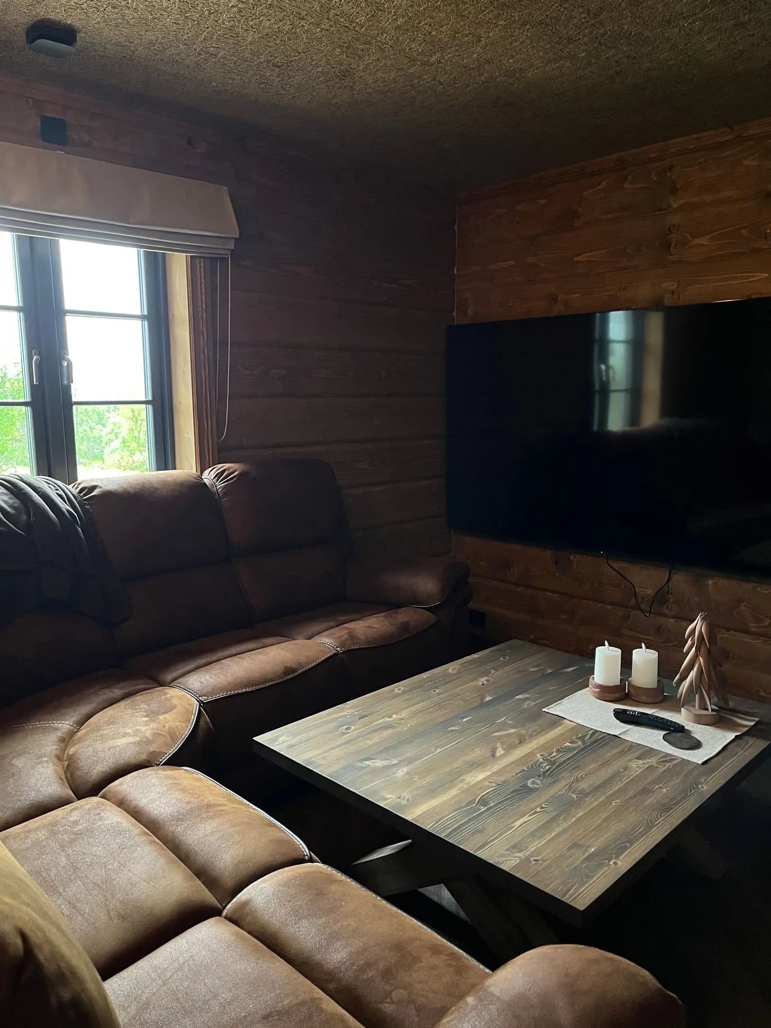 TV-stuen med stor flatskjerm-TV på tømmerveggen, brun skinnsofa og trebord — klar for filmkveld.